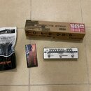 Fotografie zobrazuje sadu příslušenství značky VALETON. Je zde hnědý kartonový box s nápisy EFFECTS STRIP Mini, DAPPER Mini a VALETON, bílý sáček s n…