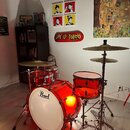 Červená průhledná bicí souprava značky Pearl. Sestává z basového bubnu s bílým předním koženem a nápisem Pearl, malého tom-tomu a snare drumu. Soupra…
