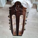 Detail hlavy klasické kytary z tmavého dřeva s viditnou masivním kresbou. Na horní části je vyrytý stylizovaný symbol připomínající písmeno C. Jsou v…