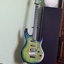 Elektrická kytara s modro-zeleným přechodovým lakem a výraznou strukturou dřeva na topu. Na hlavě je bílý nápis "Ibanez". Nástroj má dva snímače, chr…