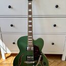 Zelená polodupová elektrická kytara s tmavým hmatníkem a bílými vložkami. Na hlavě je nápis Ibanez a ornamentální logo, na spodní části korpusu u mec…