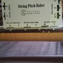 Bílá plastová nebo papírová pravítko s nápisem String Pitch Ruler přiložená k hmatníku kytary. Na pravítku jsou texty Classic Guitar, Bass Guitar, El…