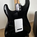 Zadní strana černé elektrické kytary s lesklým povrchem. Na kovovédesce u krku je vyryto logo Squier a nápis CE. V dolní části těla se nachází bílý p…