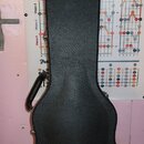 Černý tvrdý kufýr na kytaru s texturovaným povrchem. Ve spodní části je bílý nápis Gibson USA. Kufýr má připevněnou černou plastovou rukojeť a kovové…