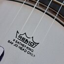 Detail bílého membrány banjona s nápisy REMO®, WEATHERKING a BANJO HEAD ONLY. Povrch je bílý s jemnou texturou, v horní části jsou vidět struny a hma…