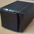 Černý, kompaktní reproduktor nebo subwoofer s hranatým tvarem a zaoblenými rohy. Na horní části je vyražený nápis "BASS" a na pravém boku je viditeln…