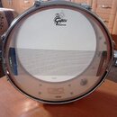 Fotografie znázorňuje přední strunu bubnu s napnutým bílým koženem a vložkou z kovové mřížky. V horní části je černé logo GRETSCH a pod ním nápis PER…