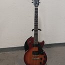 Elektrická kytara typu Les Paul v červenohnědé barvě s přechodem do tmavšího odstínu po okrajích. Na hlavě hmatníku je nápis Epiphone a pod ním kurzi…