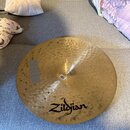 Zlatý kovový činel s viditelným kovánívým povrchem. Na spodní části je černý nápis Zildjian. V centru se nachází malá bílá nálepka s textem K Zildjia…