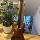 Hnědá elektrická basová kytara s dřevěným povrchem a vyfrézovaným tělem. Na hmatníku je vidět nápis "Squier". Nástroj stojí opřený o dřevěnou zábranu…