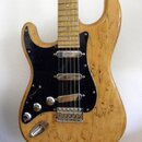 Elektrická kytara s tělem z přírodního dřeva s výraznou kresbou zrn. Má černý pickguard, tři snímače typu single-coil a chromovaný hardware. Na krytc…