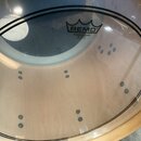Průhledná bubenová kožíška s černým kruhovým lemem. Na povrchu je černé logo REMO a nápisy POWERSTROKE®, P3 CLEAR, MADE IN U.S.A. Pod kožíškem je vid…