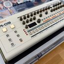 Bílá rytmická sekvenční jednotka s nápisy Roland a TR-09. Zařízení obsahuje řadu ovládacích knoflíků, posuvníků a tlačítek s označením jako BASS DRUM…