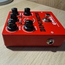 Červený kytarový efekt pedál s kovovým šasi. Na horní straně jsou čtyři černé oválné knoflíky s popisky BASS, MIDS, TREBLE a GAIN, jeden červený knof…
