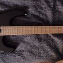 Černá elektrická kytara s hnědým hmatníkem a světle hnědou hlavou. Na hlavě je vidět logo "Cort" a nápis "X-100". Kytara má dva humbuckery, Tremolo s…