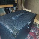 Černý kytarový kombozesilovač s povrchem z texturovaného vinylu. Na horní straně je umístena černá plastová rukojeť a v rozích jsou vidět kovové šrou…