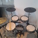 Elektronická bicí souprava značky Roland s černými rámy a bílými membránami. Na membránách jsou vidět nápisy Roland a logo V-Drums. Soubor obsahuje t…