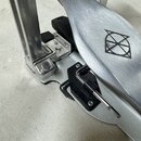 Detailní záběr na kový pedál bicího bubnu v stříbrné barvě. Na šlapce je vyryto černé logo znázorňující stylizovaný kruh s přečarovaným křížem. Mecha…