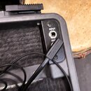 Detailní pohled na ovládací panel černého elektronického zařízení s nápisy INPUT a SEN. V konektoru INPUT je zapojen černý kabel značky RockBoard. Za…
