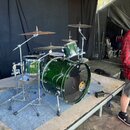 Zelená bicí souprava s lesklým povrchem umístěná na podiu. Souprava obsahuje basový buben, malý buben a tom s viditelným logem Pearl. Součástí jsou t…