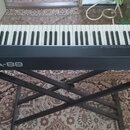 Černá klaviatura s 88 klávesami umístěná na černém X-stojanu. Na přední straně je bílý nápis Roland A-88 a v pravém horním rohu logo Roland. V pravé…