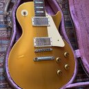 Zlatá elektrická kytara typu Les Paul v hnědém kufru s fialovou výstelkou. Nástroj má dva humbuckery v chromovaných rámečcích, bílý plech a čtyři zla…