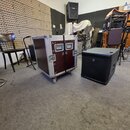 Na fotografii jsou dva přepravní kufry v interiéru s akustickými panely. Jeden je hliníkový flightcase s vínovým povrchem, kovovými hranami a zámky.…