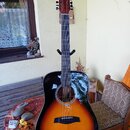 Akustická kytara s černým korpusem a přechodem do oranžové barvy v prostoru kolem otvoru. Na hlavě hmatníku je nápis FESLEY a logo ve tvaru stylizova…