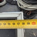Detailní záběr na hliníkový rám transportního kufru s černým povrchem. Na horním rohu rámu je viditelné opotřebení a odřasání materiálu. Přes rám je…
