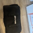 Černý polotvrdý pouzdro na hudební nástroj z textilního materiálu. Uprostřed je bílý nápis ROCKBAG a pod ním menší text by Warwick. Povrch vykazuje m…