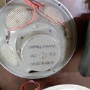 Fotografie zachycuje zadní stranu šedého reproduktoru s kovovým rámem a připojenými červenými a černými vodiči. Na centrálním magnetu je vyražen nápi…