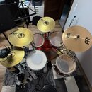 Akustická bicí souprava v červené barvě s kovovým hardwarem. Na činelech jsou vidět nápisy MEINL a modelové označení MCS. Souprava obsahuje basový bu…