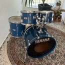 Modrá bicí souprava skládající se z basového bubnu, dvou tomů a jednoho floor tomu. Na přední straně basového bubnu je bílý nápis YAMAHA. Na levém to…