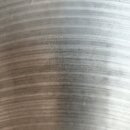 Detailní záběr na povrch kovového činelu s koncentrickými drážkami. V horní části je vyražen nápis AVERDIS / ZILDJIAN CO / GENUINE / HAND HAMMERED CY…