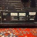 Detail zadní strany černého kytarového komba s mřížkou. Na štítku jsou uvedeny nápisy BUGERA THREE INFINIMUM, ZHONGSHAN EUROTEL ELECTRONICS LTD a Mad…