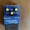 Modrý efekt pedál s nápisy Compression Sustainer a CS-2. Na horní části jsou tři ovládací knoflíky s popisky LEVEL, ATTACK a SUSTAIN a červená kontro…