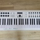 Bílá klaviatura s 61 klávesy. Na levé straně je nápis KEYLAB 61 ESSENTIAL a uprostřed logo ARTURIA. Horní panel obsahuje množství tlačítek, posuvníků…