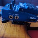 Modrý kytarový pedál s ovládacími knoflíky a displejem, umístěný na těle kytary. Na zadní straně jsou nápisy LEFT OUT (Mono), RIGHT OUT, USB a PUSH E…