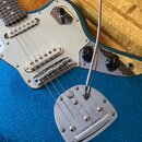 Modrá elektrická kytara s třpytivým povrchem a bílým pickguardem. Na kovovém krytu tremola je vyryto logo Fender STRATOCASTER. Nástroj má dva bílé sn…