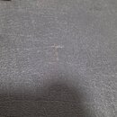 Fotografie detailu tmavě šedého povrchu z texturovaného materiálu připomínajícího kůži nebo vinyl. Povrch vykazuje drobné nečistoty a v centrální čás…