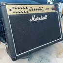 Kytarový kombo zesilovač značky Marshall v černém vinylovém potahu s bílým lemováním. Horní ovládací panel je zlatý a nese nápis JVM s řadou potencio…
