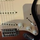 Detail elektrické kytary s bílým pickguardem a tmavě hnědým tělem. Na snímku jsou tři bílé snímače s nápisem Noiseless, jeden přepínač a tři bílé ová…