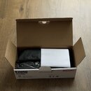 Otevřená hnědá kartonová krabice, ve které se nachází černý polstrovaný obal a bílý papírový manuál. Na přední straně krabice je nápis E205U, USB CON…