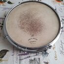 Fotografie znázorňuje buben s napnutým bílým koženým Membranem a chromovaným obručem. Na povrchu membrány je v horní části viditelné výrazné opotřebe…