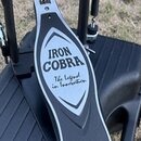 Detailní pohled na kovový pedál bicího stroje v černé barvě s nerezovým pryskem. Na prysku je vyryt nápis IRON COBRA a pod ním kurzívou text The Lege…