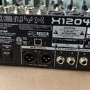 Zadní strana míchacího pultu černé barvy s nápisem XENYX X1204USB a logem behringer. Na povrchu jsou viditelné varovné texty, certifikace CE a FS, sé…