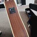 Detail hřbitu akustické kytary z hnědého dřeva s bílým lemováním. Na boku je osazený černý ovládací panel značky FISHMAN s nápisy volume, tuner, bass…