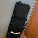 Černý textilní obal na hudební nástroj s rukojetmi a zipy. V dolní části je bílý nápis YAMAHA doprovázený logem značky v kroužku. Obal je opřen o šed…