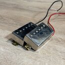 Dva elektrické snímače typu humbucker s kovovými kryty stříbrné barvy. Snímače mají v horní části viditelné šesté polské šrouby. Z jednoho z nich ved…