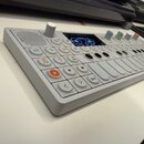 Bílá elektronická klaviatura s kontroléry a displejem. Na ovládacím panelu jsou vidět nápisy JOIN, 1-4 a Shift. Zařízení obsahuje několik bílých tlač…